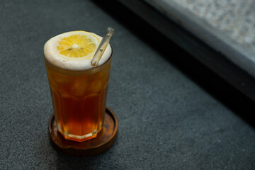 iced lemon tea drink served on transparent glass over small wooden plate on stone tile