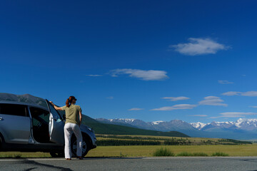 Obraz premium mature woman traveling by car stopped on the side of the road and admires the Altai mountains