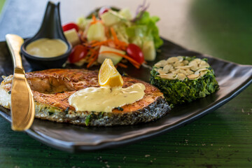 food by salmon fish steak grill lemon with nut in spinach and vegetable fruits salad with sauce on black dish and green table with gold or brass knife for seafood and omega 3 in Japanese restaurant