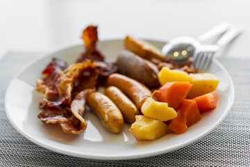 breakfast by Steamed potatoes carrot sausage and grilled bacon with spoon fork on white dish or plate and placemat for healthy food meal or cuisine in restaurant cafeteria and food court by closeup