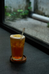 iced lemon tea drink served on transparent glass over small wooden plate on stone tile