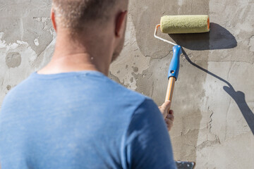A man applies primer to a concrete wall using a roller. The image shows the process of painting...