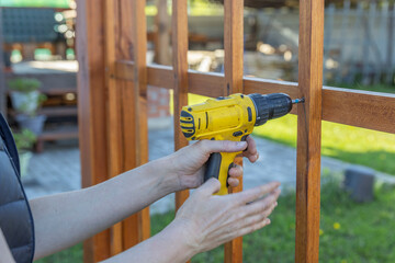 A person in work attire using a power drill to secure a wooden fence panel onto metal posts in a...