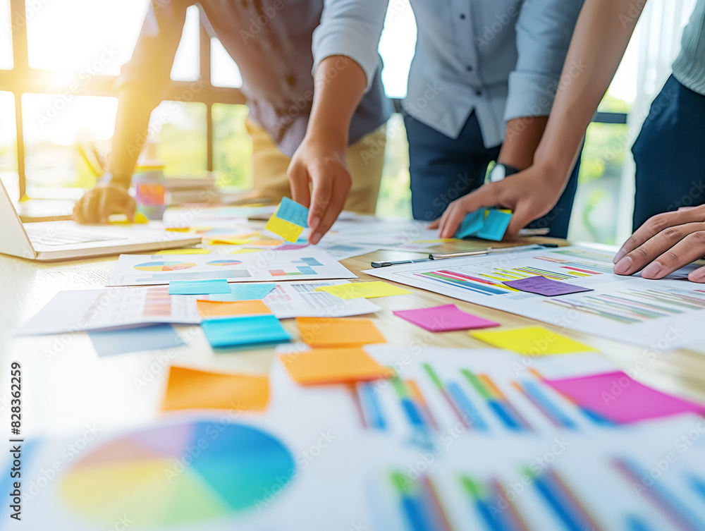 Poster people collaborating over colorful charts on a table, in a business meeting, concept of teamwork. ge