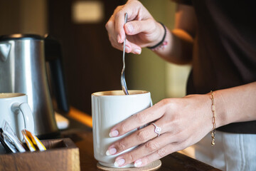 Person stirring drink in a white mug