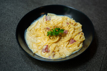 creamy smoked beef spaghetti carbonara served on black plate, over stone tile background