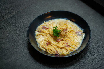creamy smoked beef spaghetti carbonara served on black plate, over stone tile background