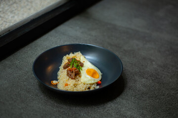 beef saikoro rice bowl and sunny side up egg on black plate, over stone tile