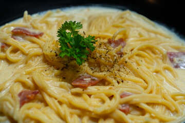 creamy smoked beef spaghetti carbonara served on black plate, over stone tile background