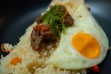 beef saikoro rice bowl and sunny side up egg on black plate, over stone tile