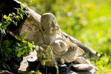 Laughing Buddha figure. Lucky Buddha leaning on a tree trunk in the open air.