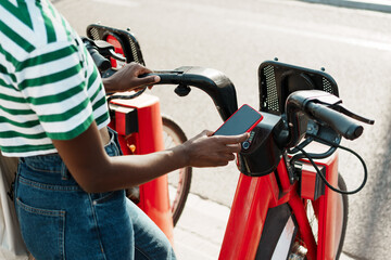 Hand of black woman renting a red bicycle in a bike rental station with mobile app