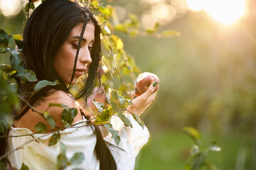 Beautiful young female with delicious harvested apple in sunlight. Side view of pensive woman with...