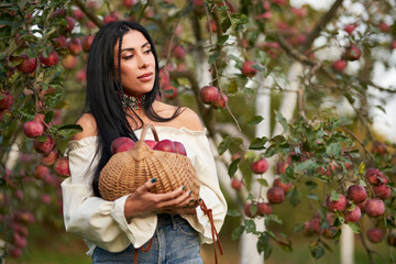 Cute farmer woman with freshly harvested apples in handbasket. Portrait of thoughtful lady in...