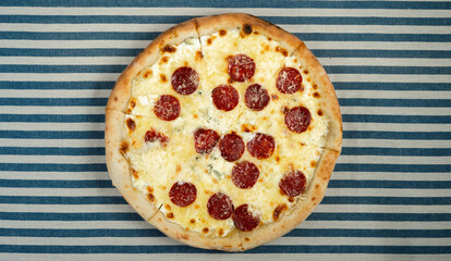 Pizza with smoked sausage, parmesan cheese and sauce served on a striped tablecloth in a pizzeria...