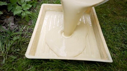 Paint is poured from a bucket into a tray. Painting the exterior of the house, paint is poured into...