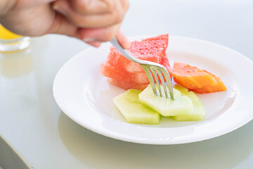 Person picking up melon slice from plate of assorted fruits