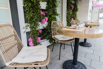 Empty wooden tables and chairs with pink decorative flowers adorn the facade of a summer street cafe