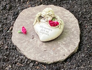 Herz mit Engel und Blumen auf dem Friedhof auf einem Grab mit Inschrift : Wir werden dich nie...