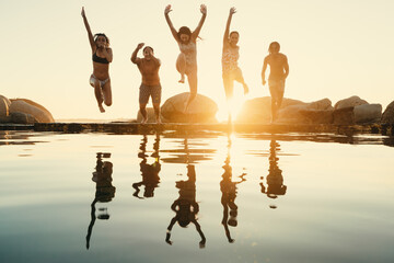 Group of friends enjoying good times and travel by jumping into water at sunset