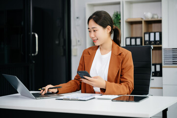 Asian woman using laptop and tablet while sitting at her working place.