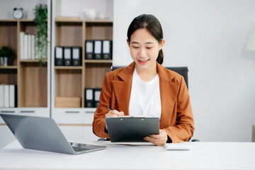 Asian woman using laptop and tablet while sitting at her working place.