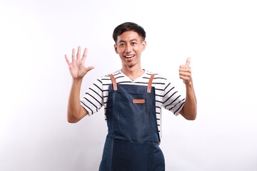 Asian young man wearing apron over white background showing six fingers with exited and happy face...