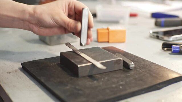 A jeweler uses a hammer to hammer out a unique ring design with a metal stamp. Craft in a jewelry workshop