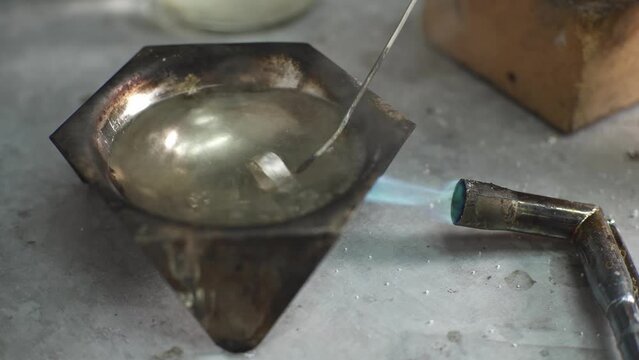 A jeweler heats a piece of jewelry with a burner in a solution of citric acid. Craft in a jewelry workshop