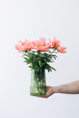 A guy holds a vase with peonies in his hands