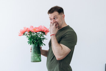 A guy holds a vase with peonies in his hands