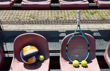 a tennis racket, balls and a volleyball on a bench on the sports tribune