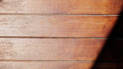 Hardwood texture background with sunlight shining diagonally from top to bottom with a brown-red...
