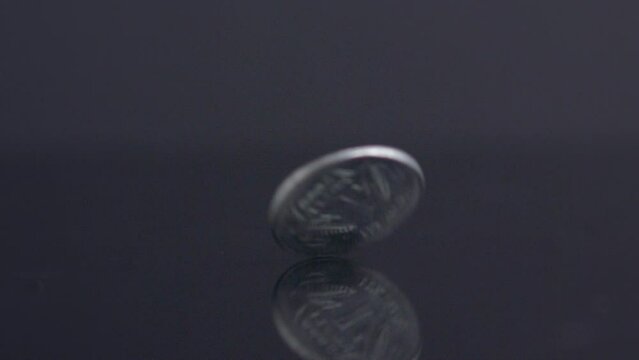 Closeup footage of 1 rupee silver coin rolling on a reflective surface isolated on a dark background