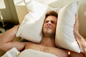 Man, frustrated and pillow on head in bed on weekend morning for insomnia, depression or mental...