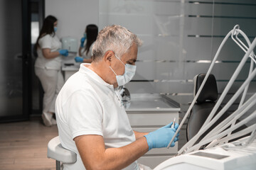 A dentist, wearing a mask and gloves, is sitting in a dental chair