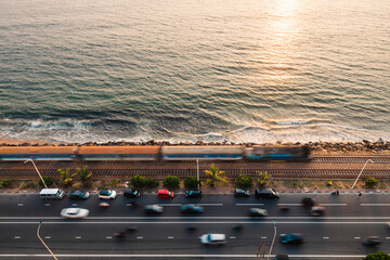 Road and railway track along coast at sunset over Indian ocean. Train arriving in Colombo, Sri...