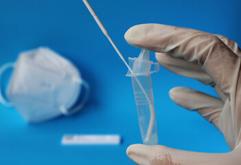 A gloved hand holds a plastic tube with a white test stick immersed in the bottom of the tube. ...