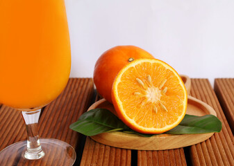 Half oranges are placed in front of one another in a wooden tray next to a glass of orange juice on a white background.


