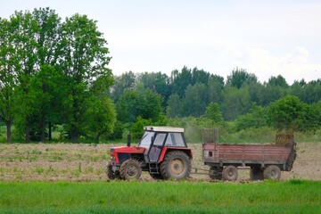 A red tractor with a trailer drives through a plowed field