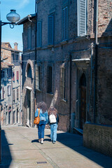 Two women walking down the street in the historic center of Urbino, Italy