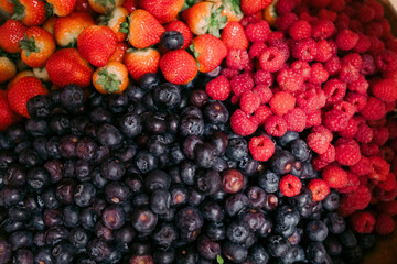 a wooden bowl filled with assorted blueberries, raspberries, strawberries