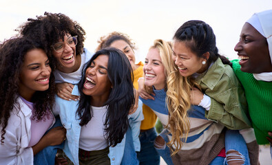 Large group of young different races only women friends standing having fun piggyback outdoors....