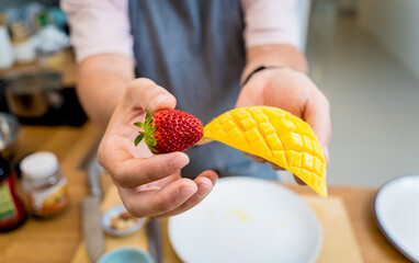 Chef at the kitchen preparing bowl of oats with strawberries and mango