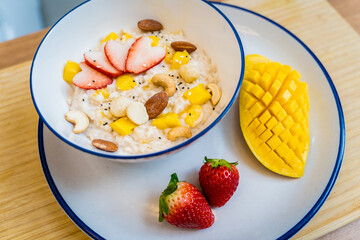 A bowl of oats with strawberries and mango arranged on a plate