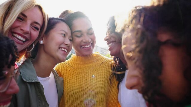 Group of multicultural young only women standing hugging in circle laughing and looking each other outdoor. Gen z female community people embracing together having fun and enjoying girls friendship