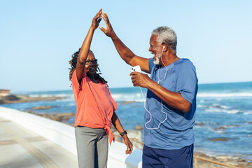 Mature couple celebrating fitness with a high five on coastal walk