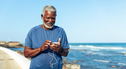 Senior man staying active by the seaside using phone during a jog