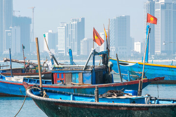 View of traditional Vietnamese fishing boats with flags on the background of the city on sunny day....