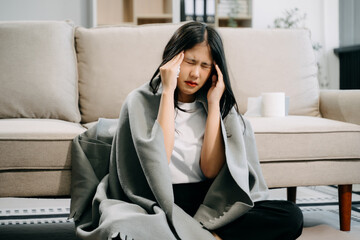 Young Asian woman suffering from flu symptoms, covered with a blanket on a sofa. Concept of...